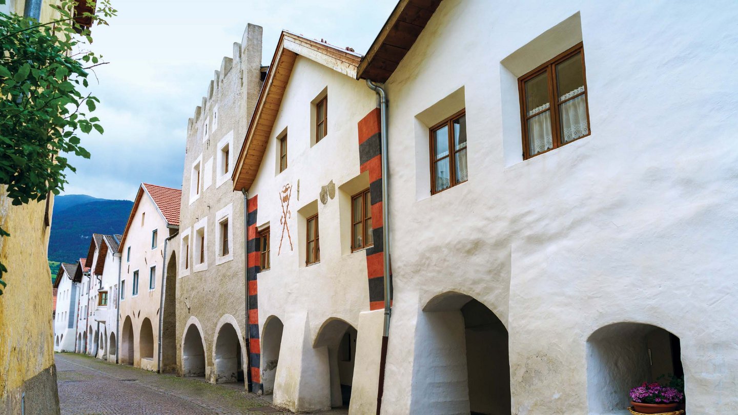 The historical white facades of Glurns line a tranquil alley, whispering tales of yore, beckoning for a leisurely stroll.